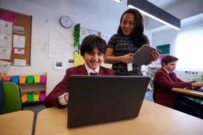 Student using laptop being overseen by teacher