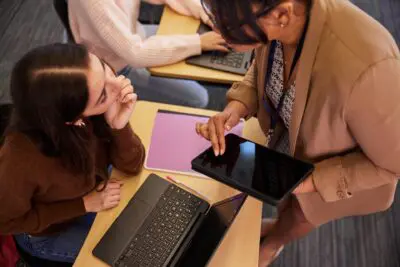 Teacher using tablet while student uses laptop